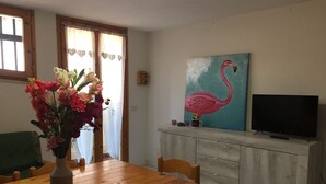 A dining area with a wooden table, chairs, a vase of flowers, a painting of a flamingo, and a television on a cabinet. - semi-detached house n residential area (Quartu Sant'Elena)