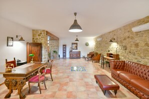 Uma sala ampla com uma mesa de jantar de madeira, cadeiras, um sofá de couro e uma parede decorativa em pedra.