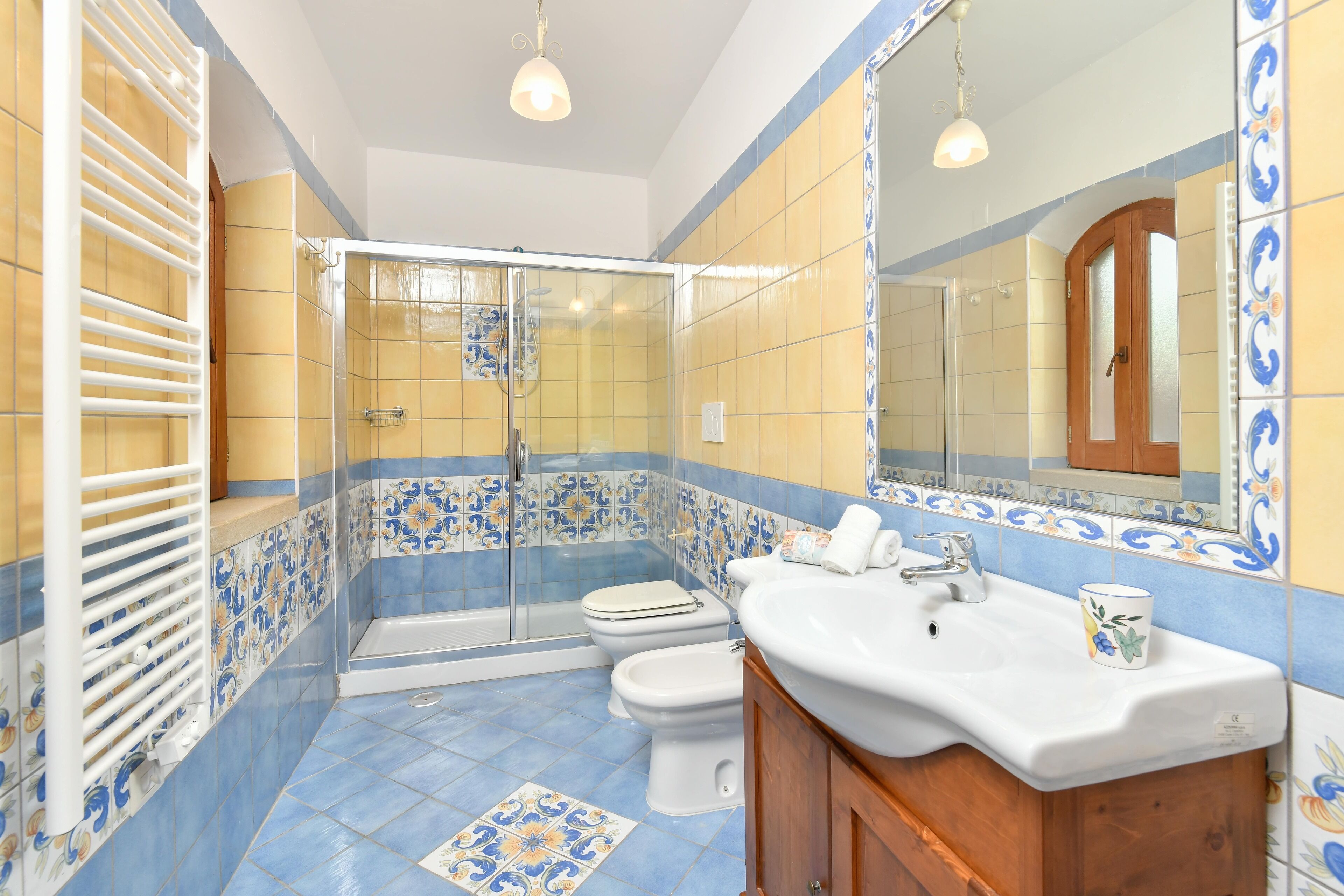 A bathroom with a shower, toilet, and sink, featuring blue and yellow tiles and wooden cabinets.