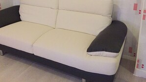Un sofá blanco con cojines negros en una habitación con paredes y suelo de tonos claros.