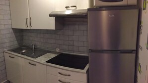 Una cocina compacta con armarios blancos, un refrigerador de acero inoxidable y un lavamanos negro.