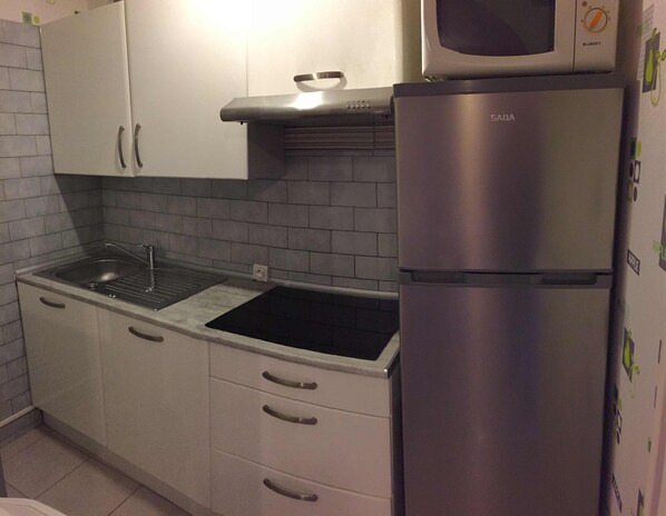 A compact kitchen with white cabinets, a stainless steel refrigerator, and a black sink.