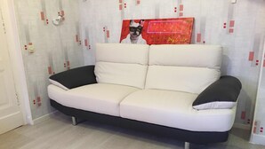 Un sofá blanco con cojines negros en una habitación con suelo de madera clara y papel tapiz estampado.
