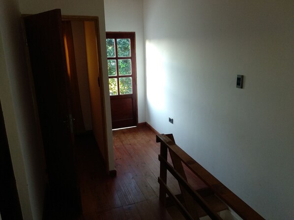 A narrow hallway with a wooden bench, a door leading to a room with a window, and a wall-mounted light switch.