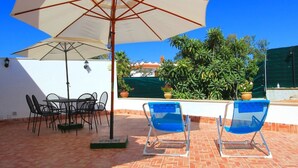 A patio with a table and chairs, a large umbrella, and a poolside area with lounge chairs.