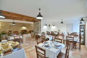 Uma sala de jantar com várias mesas postas para refeições, cadeiras de madeira e luminárias pendentes.
