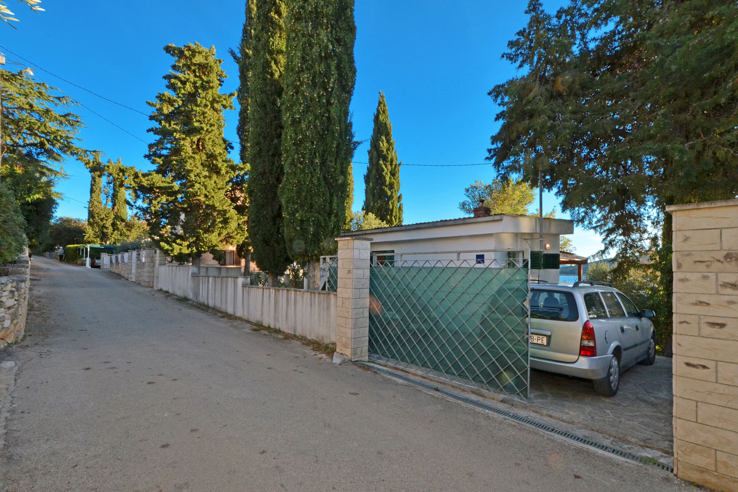 A gated parking area with a car parked inside, surrounded by tall trees and a clear blue sky.