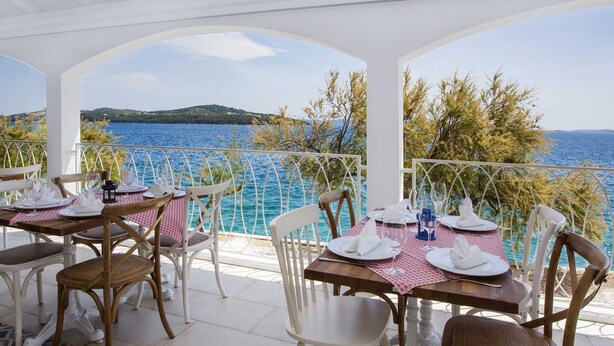 Terraza con mesas dispuestas para comer, con vistas a un cuerpo de agua y colinas.