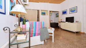 Una sala de estar con una mesa de centro de vidrio, un armario blanco, un televisor y obras de arte en las paredes.