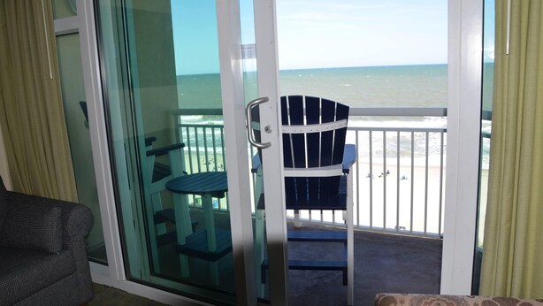A room with a sliding glass door leading to a balcony with a view of the ocean.