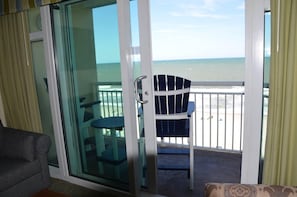 A room with a sliding glass door leading to a balcony with a view of the ocean.