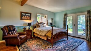 A bedroom with a large bed, a leather armchair, a nightstand, and a window with curtains.