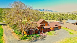 A ranch-style house with a large garage, surrounded by trees and open fields.