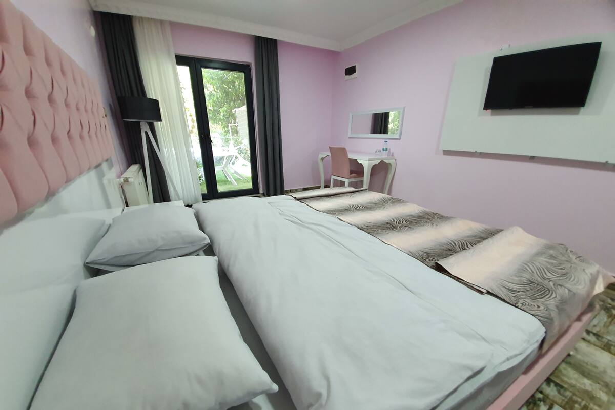 Ein Hotelzimmer mit Bett, Schreibtisch, Stuhl, Fernseher und einem Fenster mit Vorhängen.
