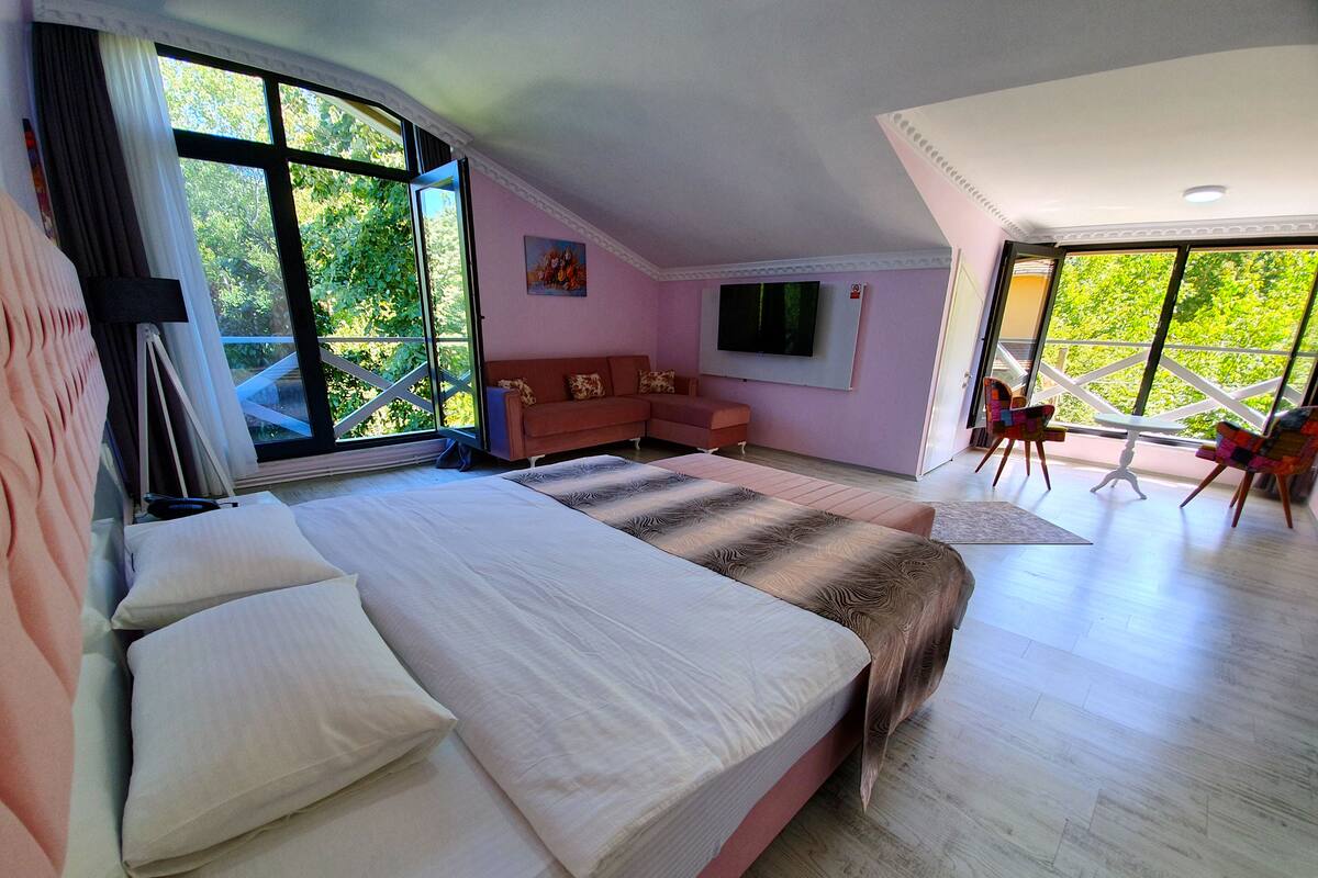 Ein Schlafzimmer mit einem großen Bett, einer Couch, einem Fernseher und einem Balkon mit Stühlen.