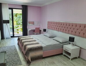 Une chambre à coucher aux couleurs rose et blanc, avec un grand lit doté d’une tête de lit capitonnée, un bureau et une chaise.