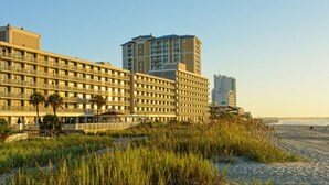 A beachfront hotel with multiple floors, a beach in the foreground, and a pier extending into the ocean. - July 4th Week - Ocean Front 1 Bedroom Deluxe Westgate Myrtle Beach Resort (Myrtle Beach)