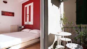 Ein Schlafzimmer mit Bett, weißer Wand, rotem Tür und Fenster mit grünen Fensterläden.