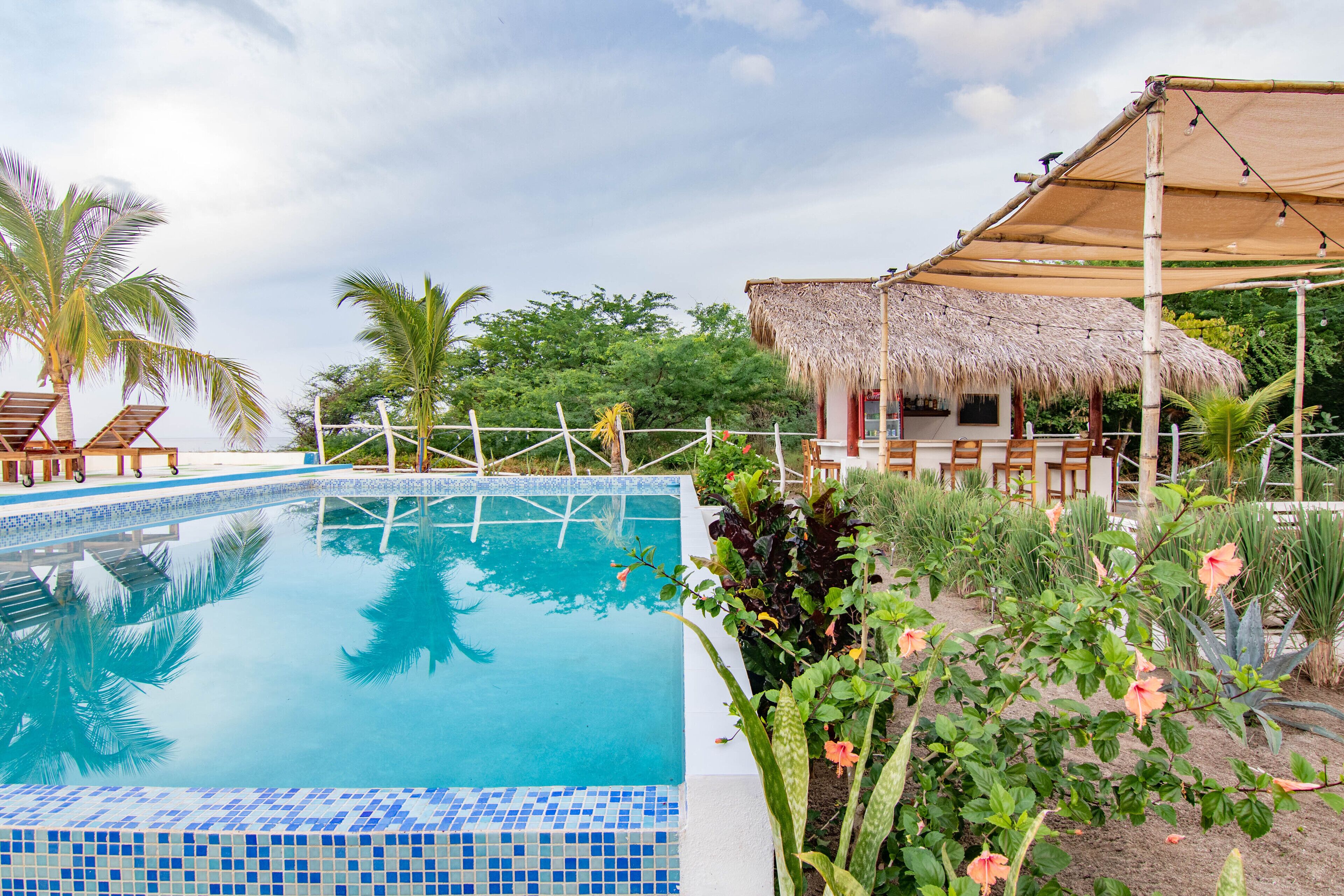 A swimming pool with lounge chairs and a thatched-roof structure.