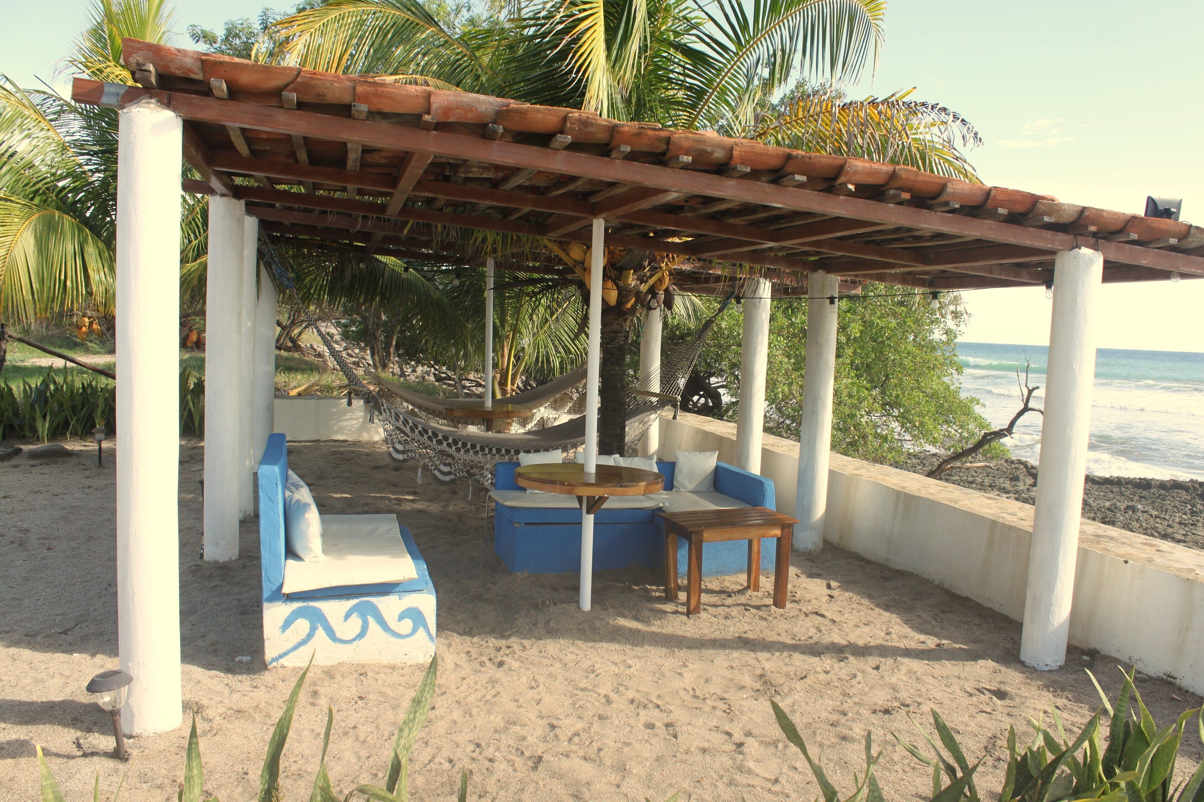 Eine Strandlounge mit einer Hängematte, blau-weißer Möbel und Blick aufs Meer.