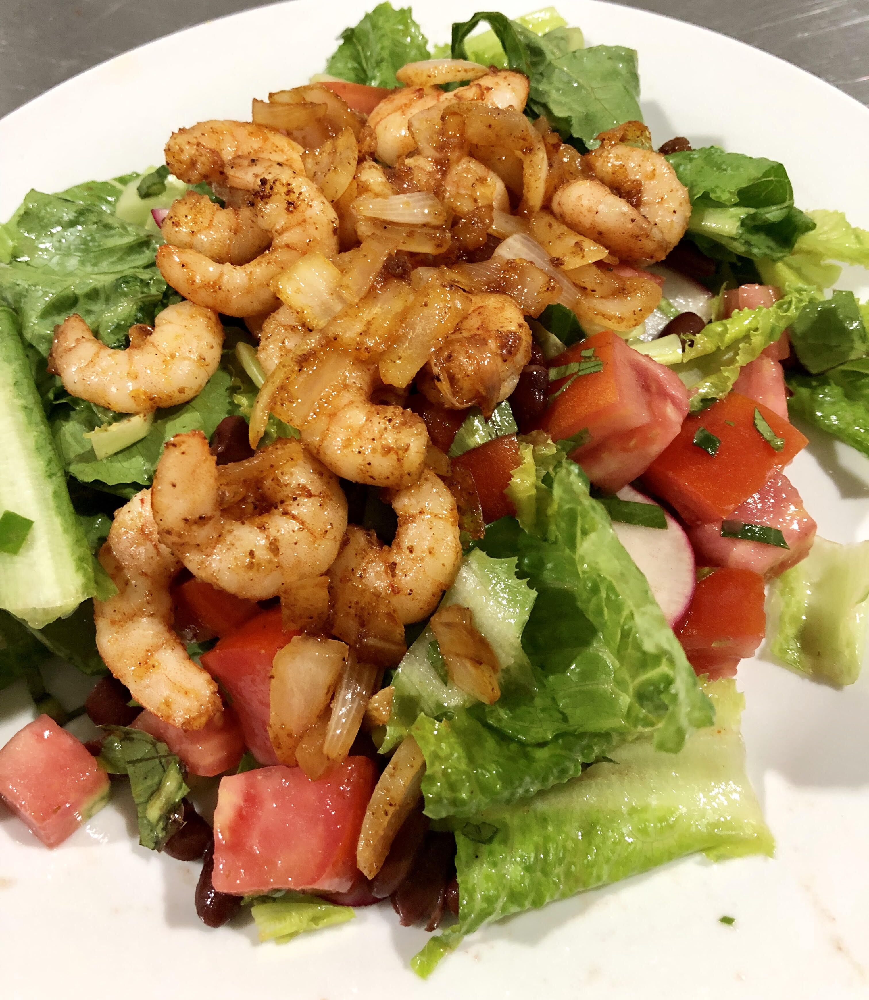 A plate of shrimp salad with lettuce, tomatoes, and onions.