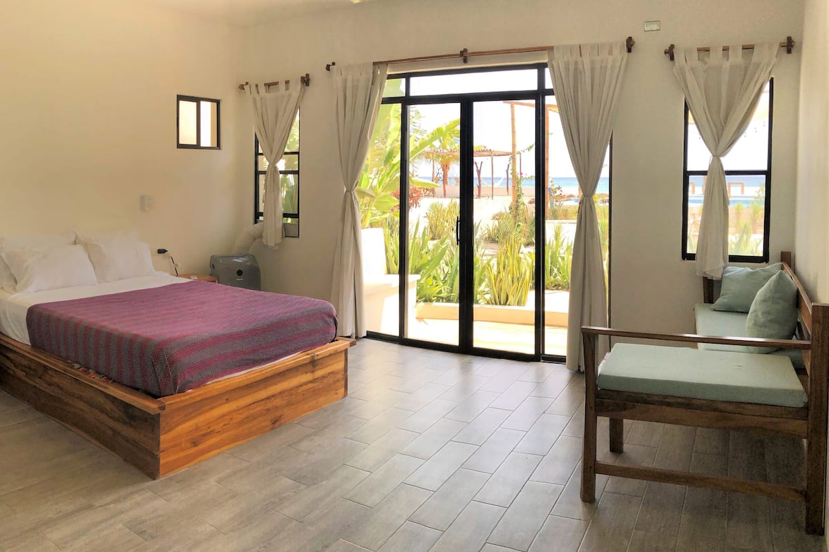 A bedroom with a wooden bed, a nightstand, a chair, and a view of the outdoors through a sliding glass door.