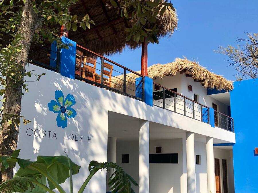 A two-story building with a thatched roof, a blue and white color scheme, and a sign reading "COSTA OESTE".