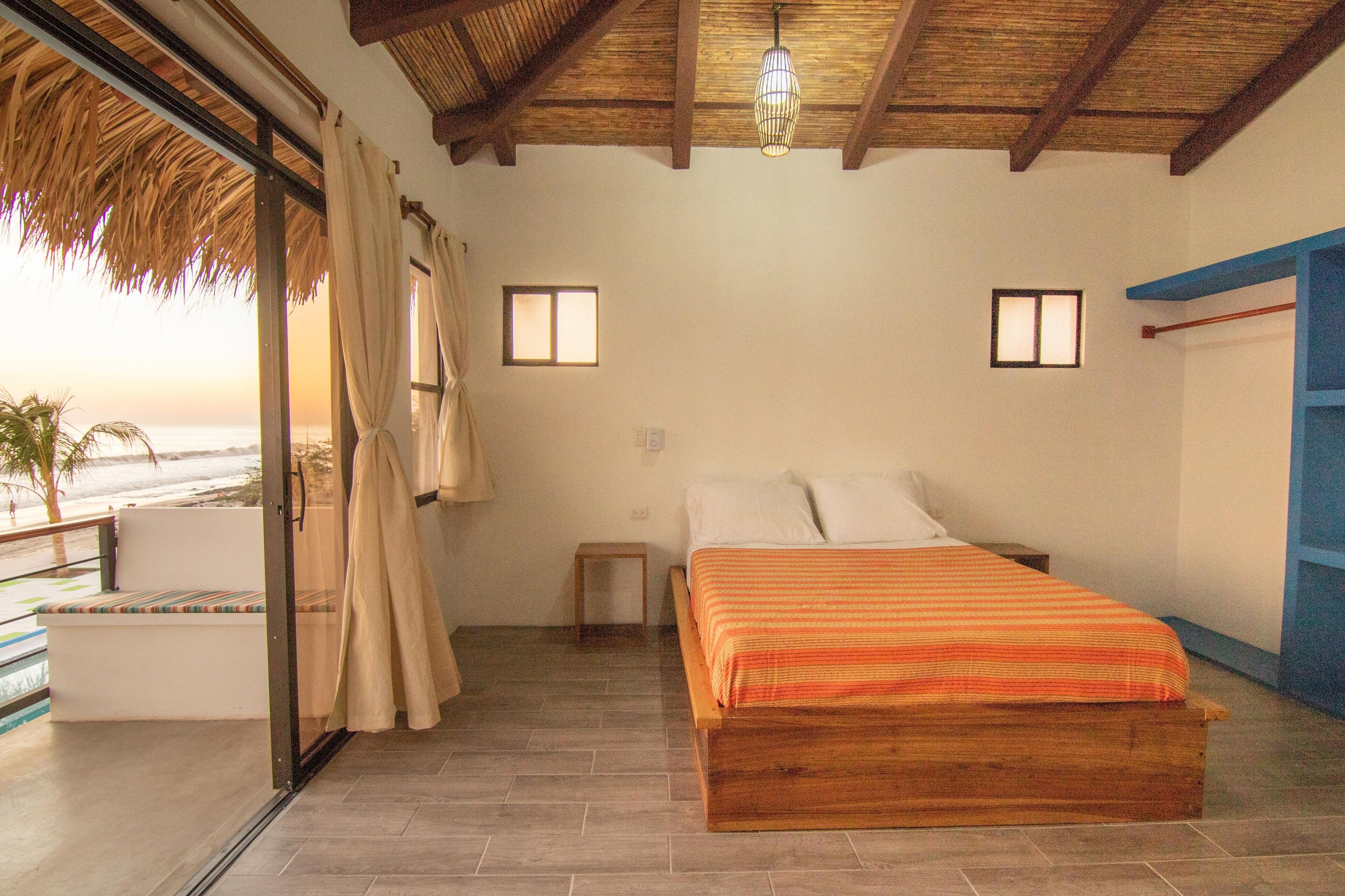 A bedroom with a wooden bed, a small bedside table, and a view of the beach through a glass door.