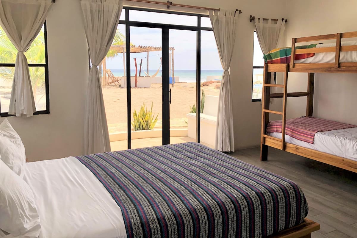 A room with a large bed, a bunk bed, and a view of the beach.