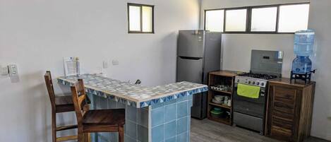 Une cuisine compacte dotée d’un îlot central carrelé, d’une cuisinière à gaz, d’un réfrigérateur et d’un distributeur d’eau.