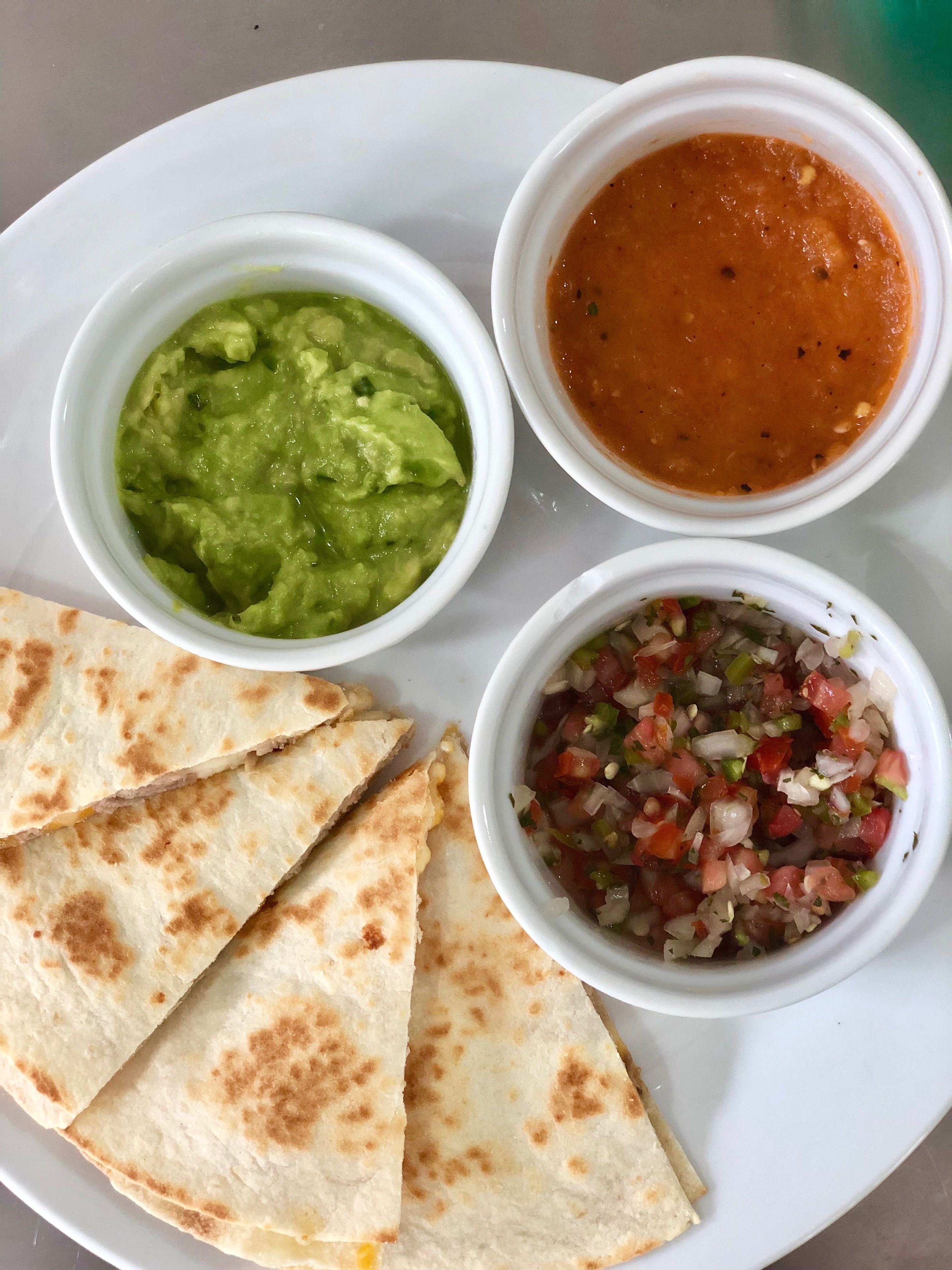 A plate with three bowls of food and four quesadillas.
