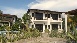A two-story building with a tiled roof, large windows, and a stone-paved entrance area with tropical plants. - Costa Oeste (Popoyo)