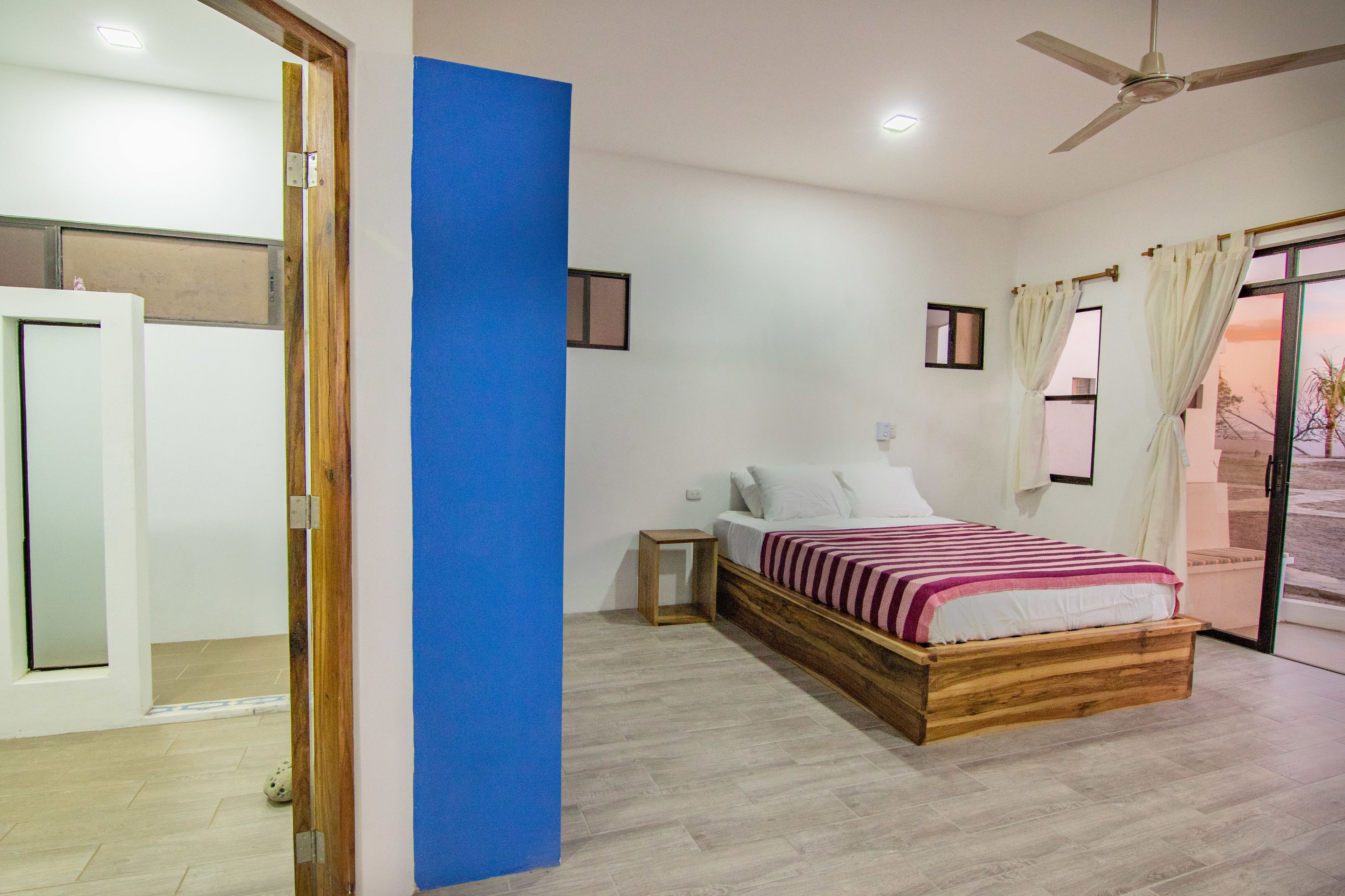 A bedroom with a wooden bed, a small bedside table, a ceiling fan, and a view through a glass door.