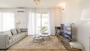 Una sala de estar moderna con un sofá, dos mesas auxiliares, un televisor y un ventanal con cortinas.