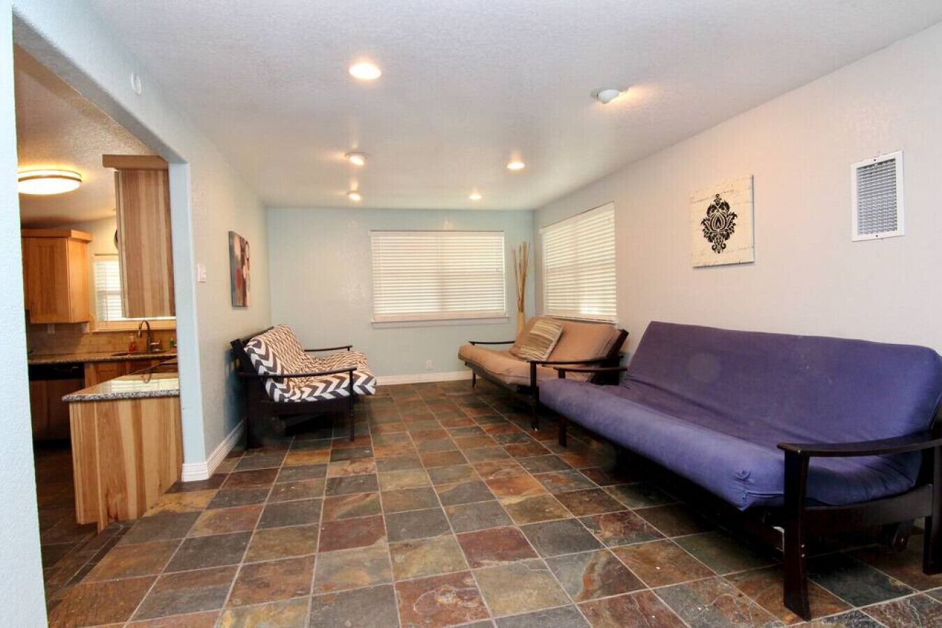 Un espacio habitable compacto con cocina, un sofá morado y un sillón estampado.