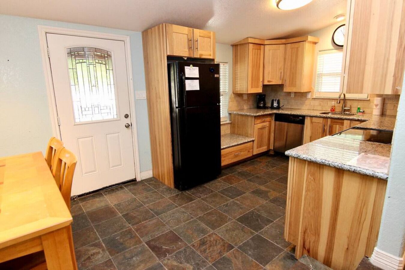 A compact kitchen with wooden cabinets, a black refrigerator, granite countertops, and a tiled floor.