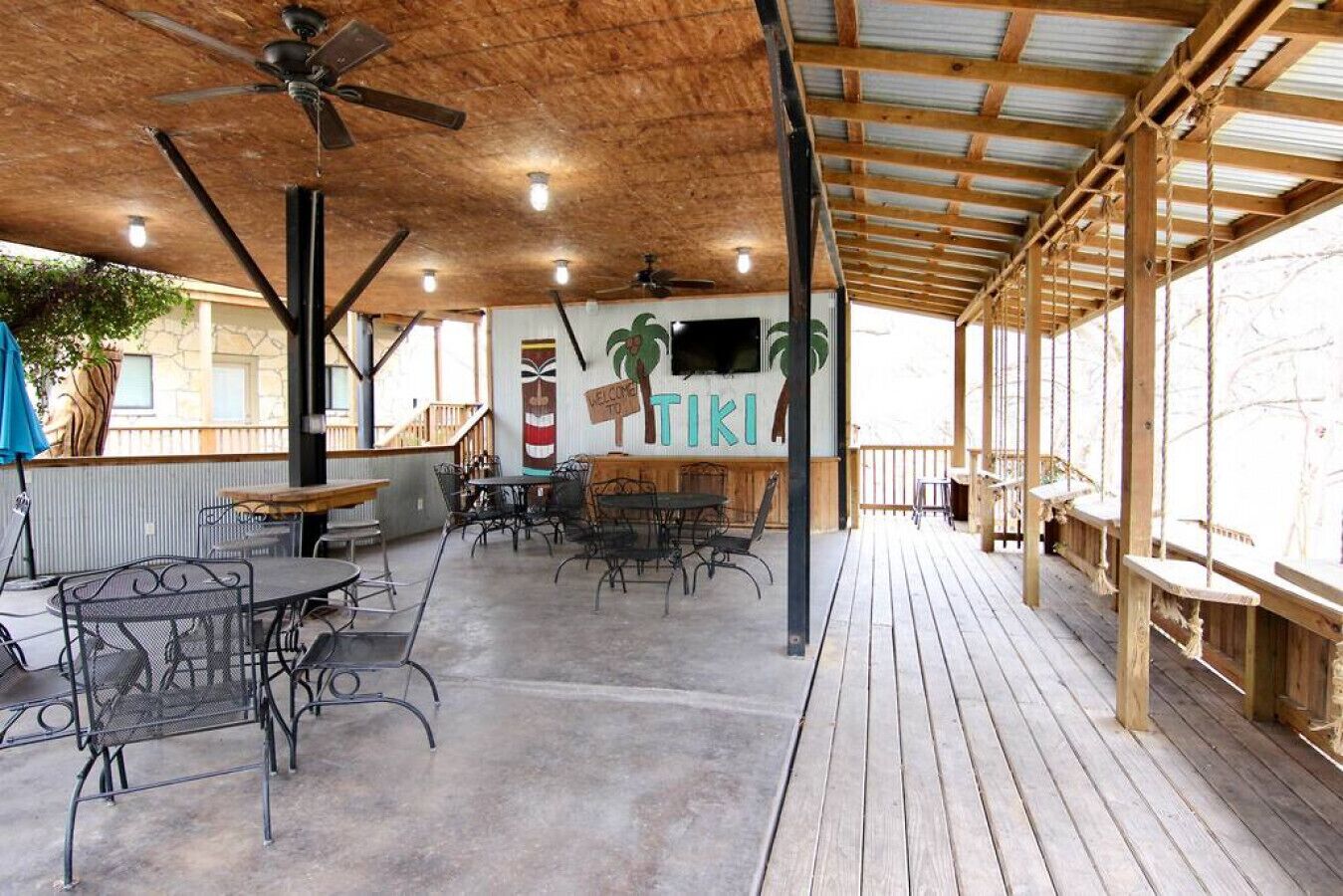 An outdoor patio area with tables and chairs, a wooden deck, and a ceiling fan.
