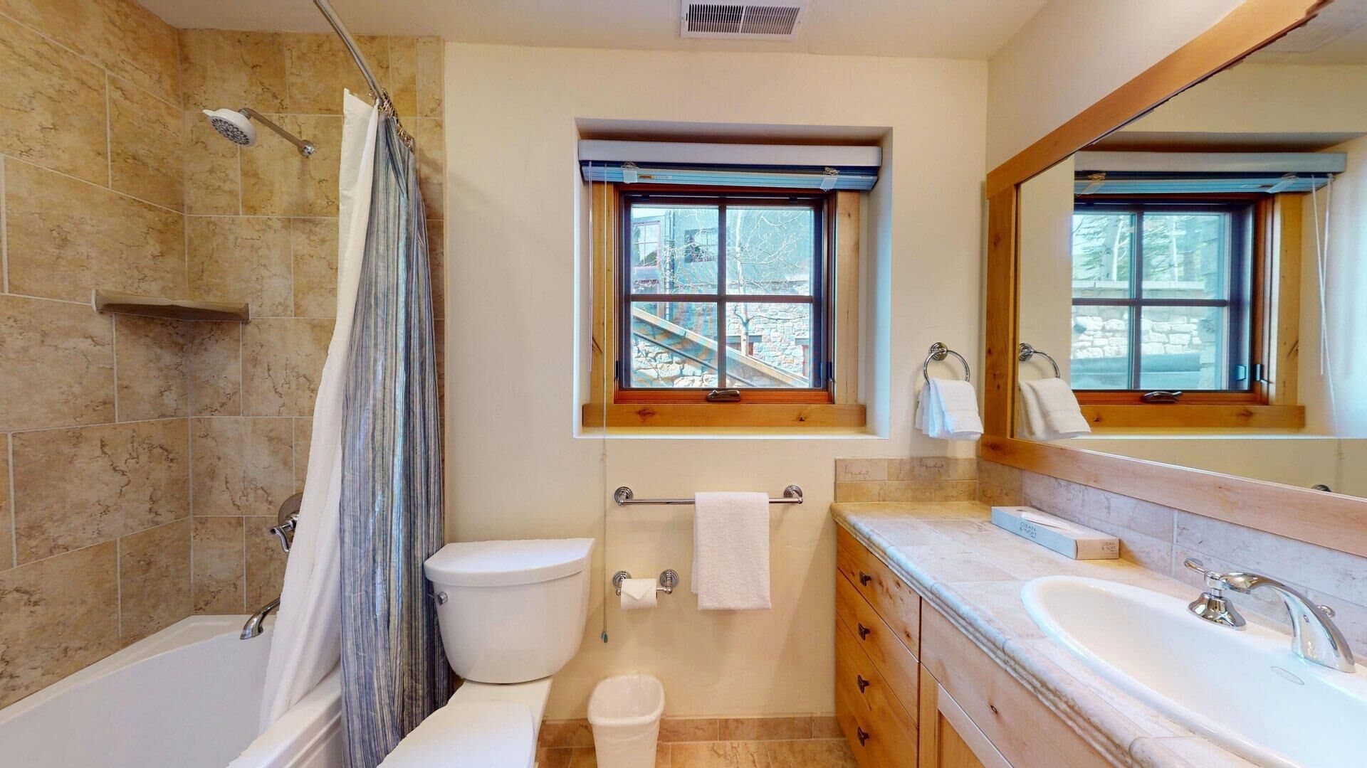 Un bagno con doccia, servizi igienici, lavandino e una finestra vista su un edificio in pietra.