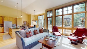 A spacious living area with a sofa, red chairs, a coffee table, and large windows offering a view of the outdoors. - Angani Way Townhome 102 -Beautiful Space! Tesla Charger in the Garage (Elkhorn)