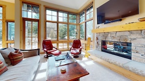 A room with large windows, a stone fireplace, and two leather chairs. - Angani Way Townhome 102 -Beautiful Space! Tesla Charger in the Garage (Elkhorn)