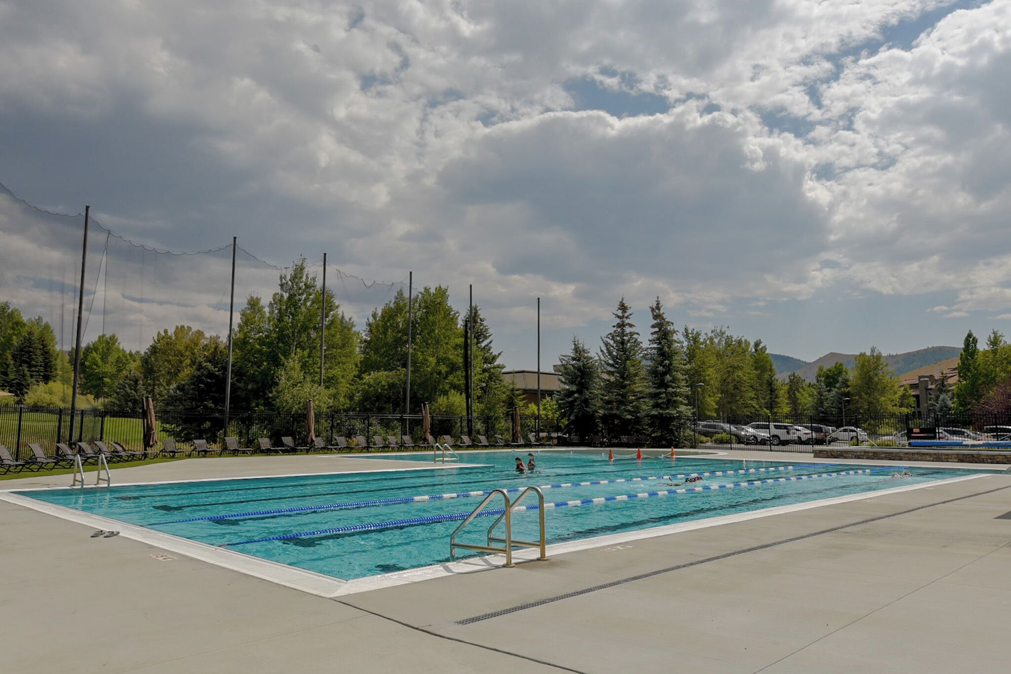 A swimming pool with lane dividers, surrounded by trees and a cloudy sky.