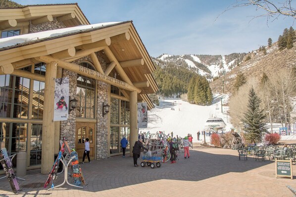 A lodge with large windows and a stone facade, surrounded by a snowy mountain landscape.
