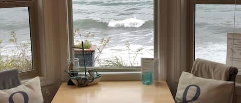 Una stanza con vista sull'oceano tramite ampie finestre, un piccolo tavolo con il cartello della vasca idromassaggio e due poltrone con cuscini decorativi.