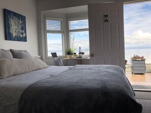 Una camera da letto con un letto grande, vista sul mare attraverso una finestra e un'uscita verso una zona esterna.
