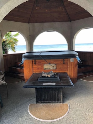 A covered outdoor seating area with a grill, wooden walls, and a view of the ocean.