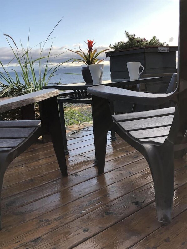 A wooden deck with a table and chairs, overlooking a body of water. - Beachfront duplex Cottage (Qualicum Beach)