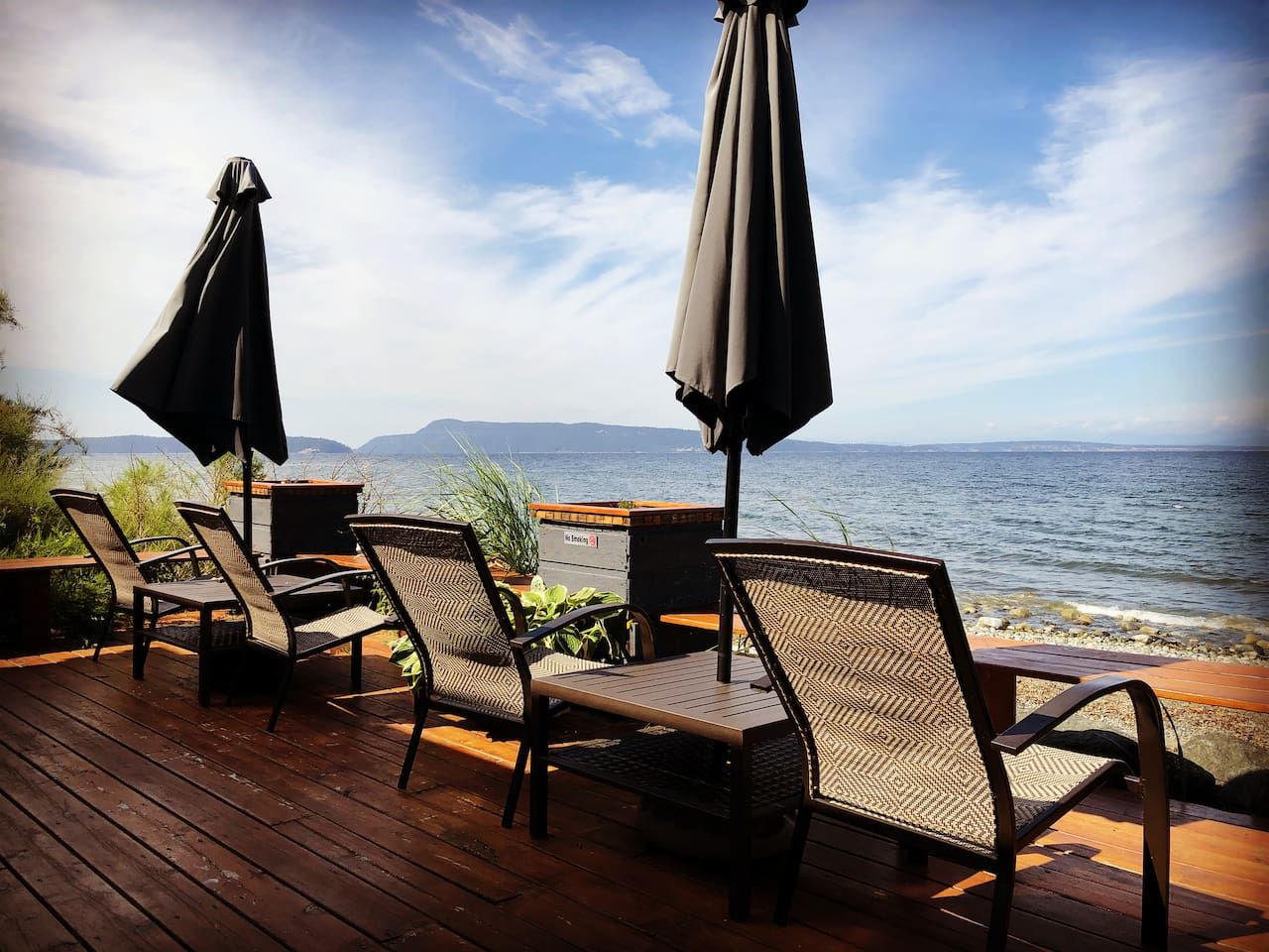 A deck with wicker chairs and tables, overlooking a body of water with distant land.