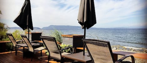 A deck with wicker chairs and tables, overlooking a body of water with distant land.