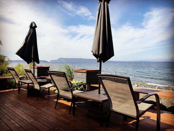 A deck with wicker chairs and tables, overlooking a body of water with distant land.