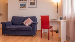 Una habitación con un sofá azul, una silla roja, un escritorio y cuadros en la pared.